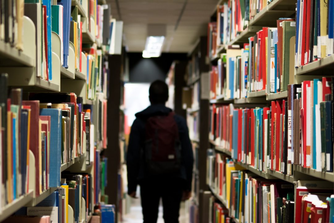 Student walking through the library past shelves of books